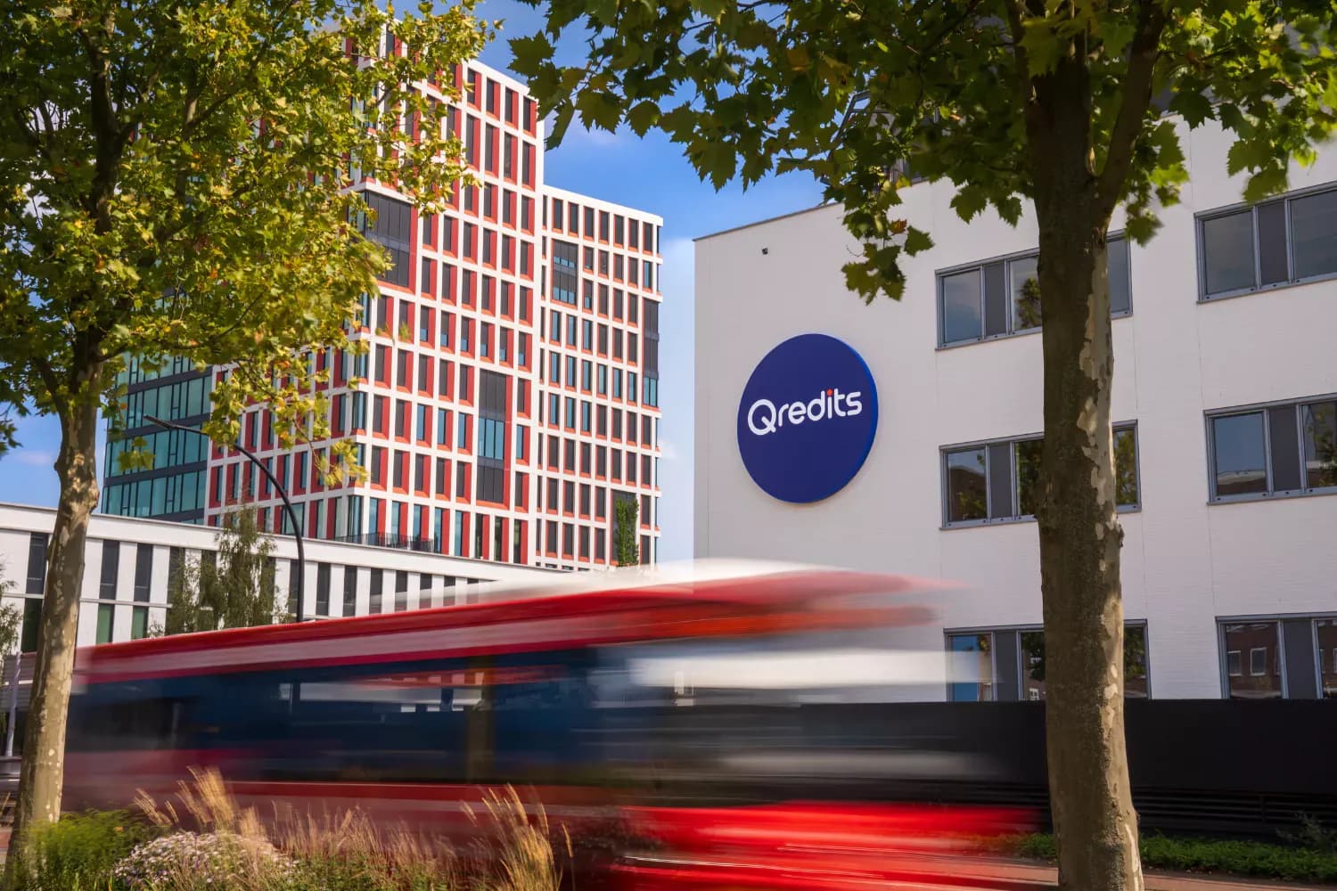 Kantoorgebouw van Qredits met groot logo op de gevel en een voorbijrijdende bus, als beeld bij de Qredits case