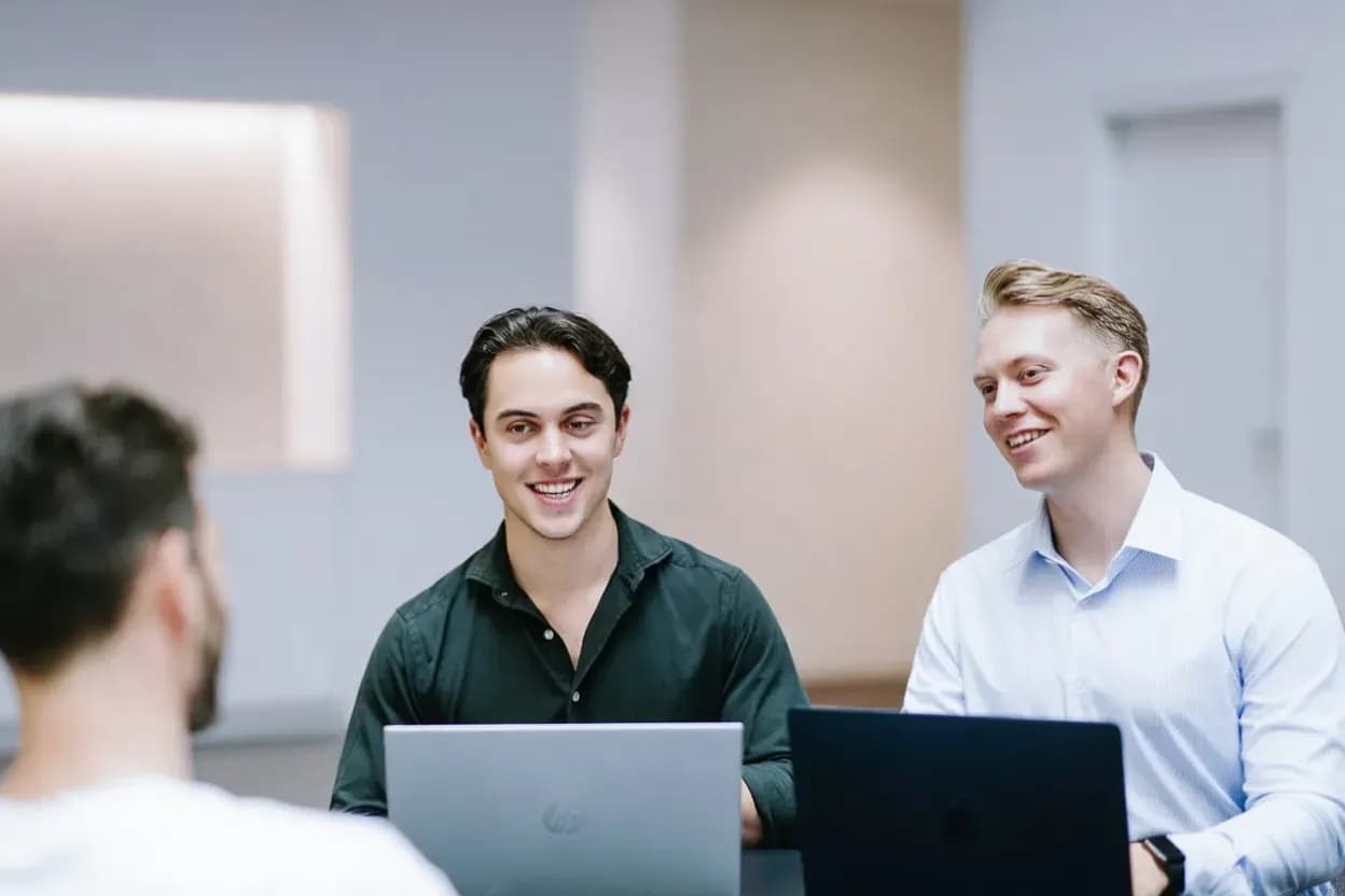 Twee PromptGorillas consultants luisteren aandachtig naar een klant tijdens een gesprek met laptops op tafel