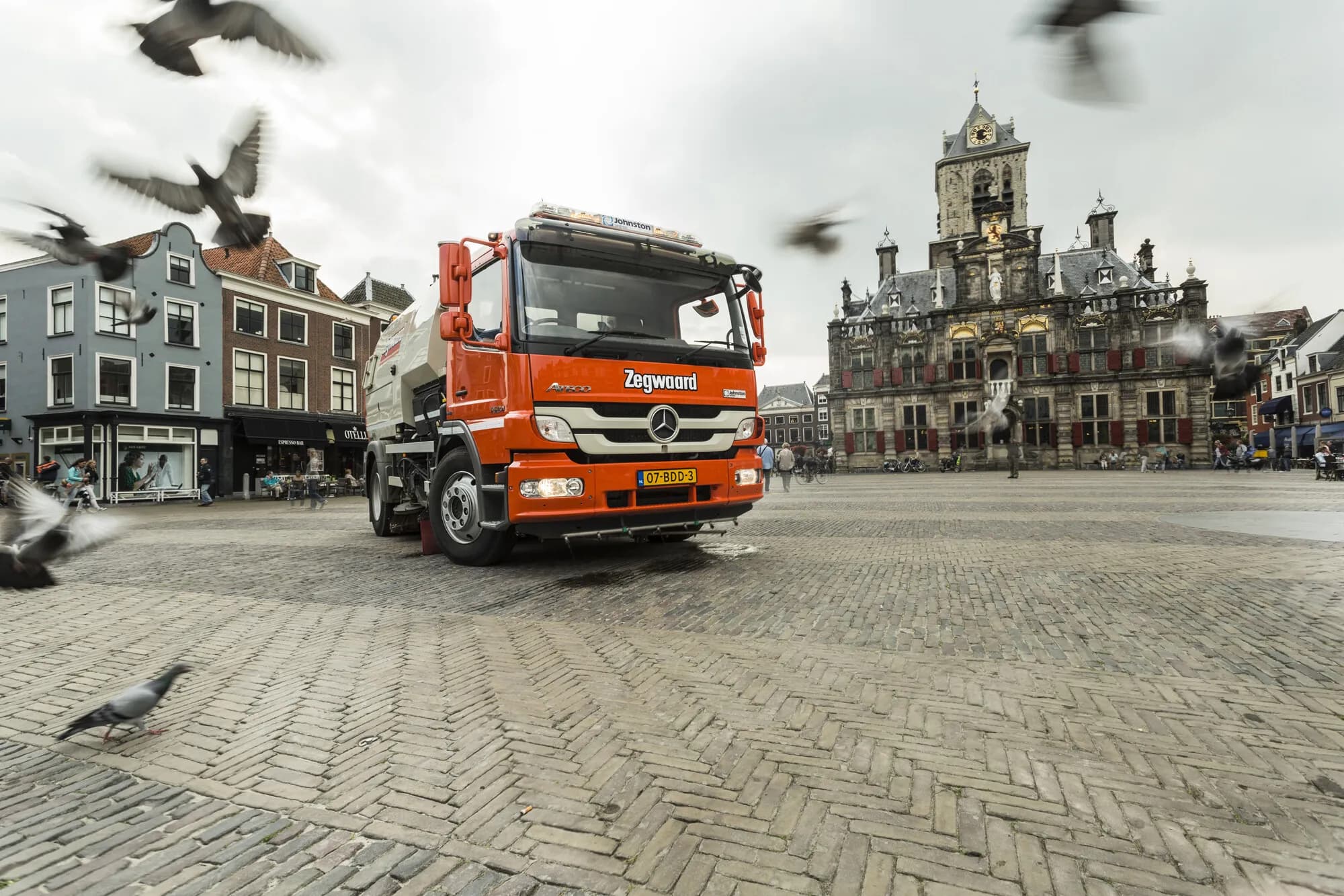Oranje Zegwaard veegwagen op de Markt in Delft met opvliegende duiven en het stadhuis op de achtergrond, als beeld bij de Zegwaard case